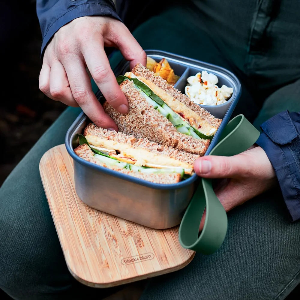 Person with lunchbox on knee taking out a sandwich