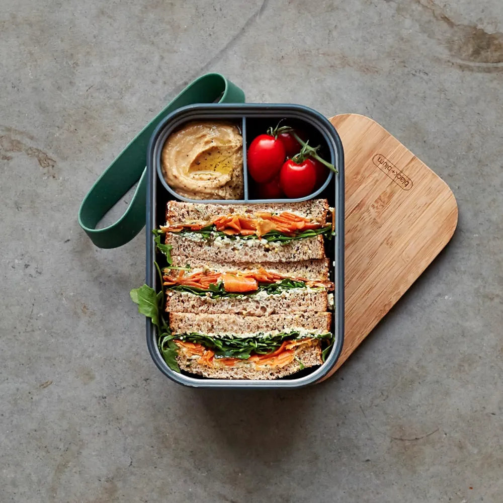 Overhead view of lunchbox with food on bamboo lid and silicone strap