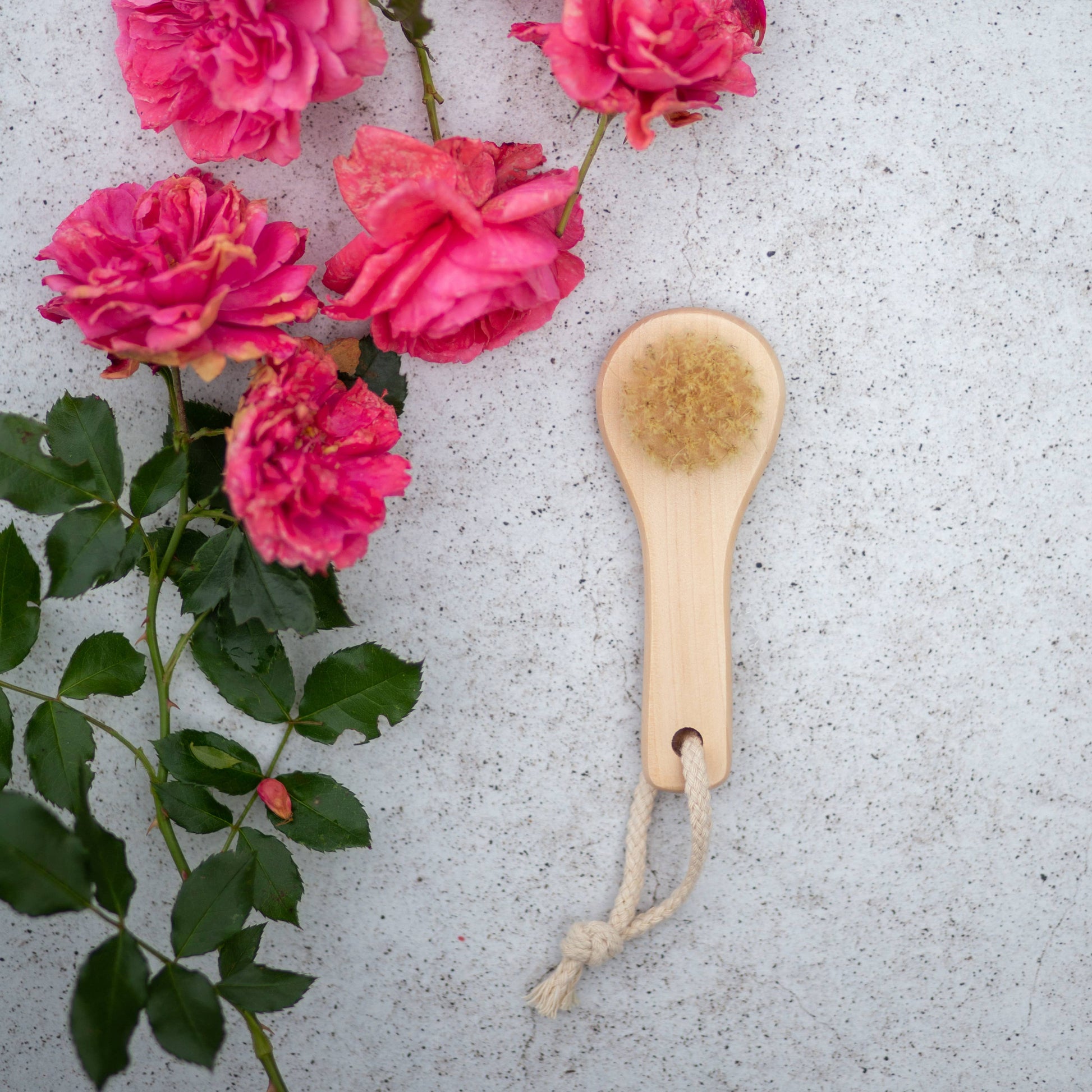 Wooden handles facial cleansing brush with natural bristles by Croll and Denecke on a gray surface with pink flowers and green leaves.