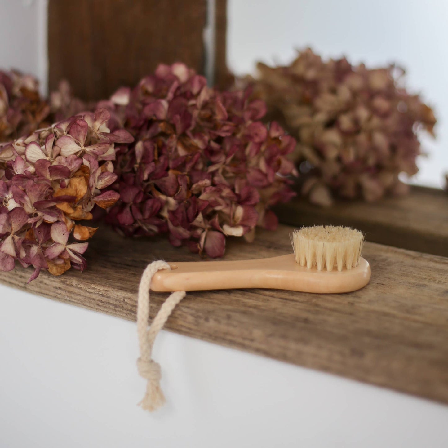 Wooden handled facial cleansing brush brush with natural bristles by Croll and Denecke on a wooden board with dried flowers and pinecones.