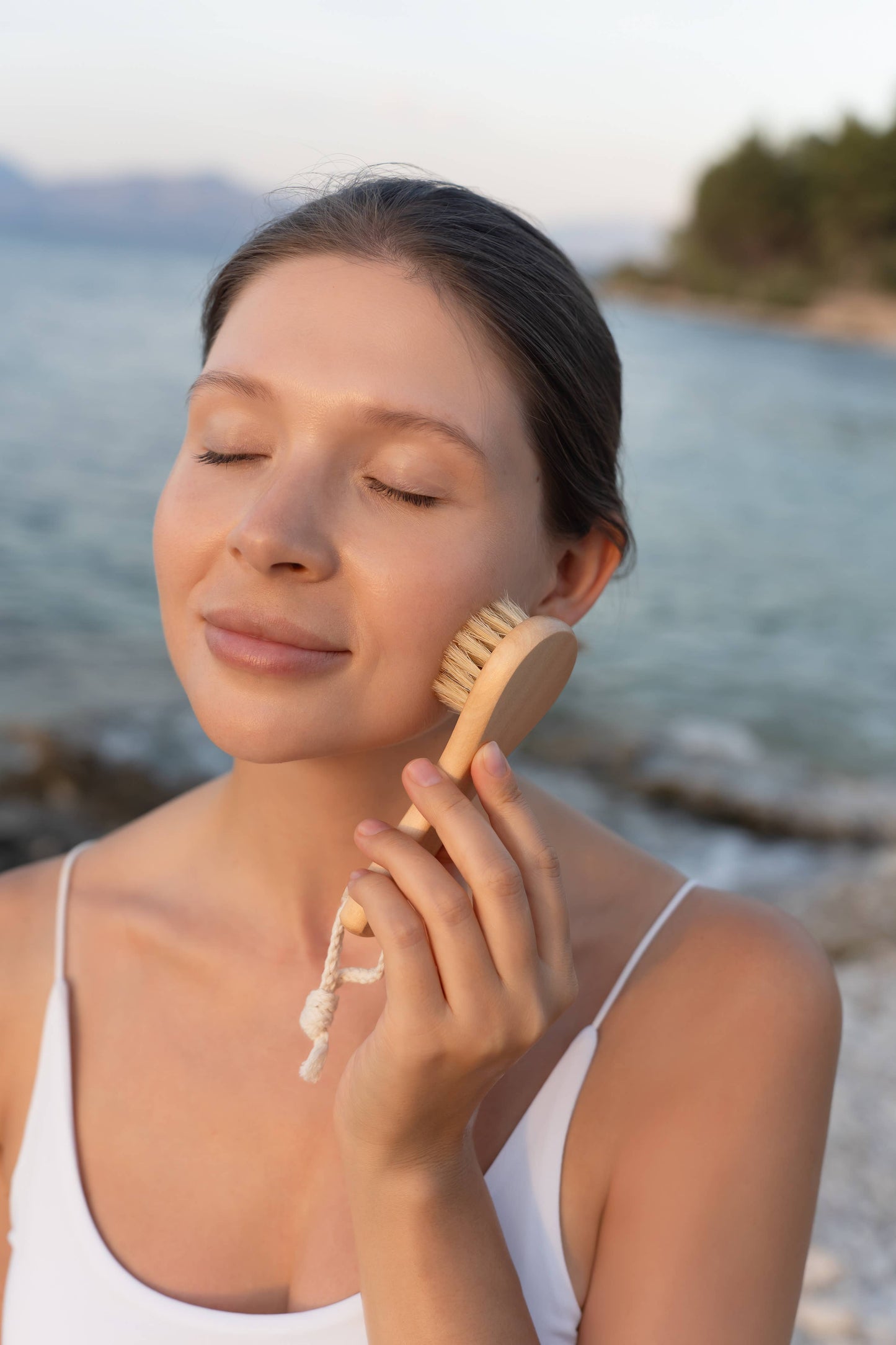 Woman using a Croll and Denecke facial cleansing wooden handled brush on her face with a blurred natural background