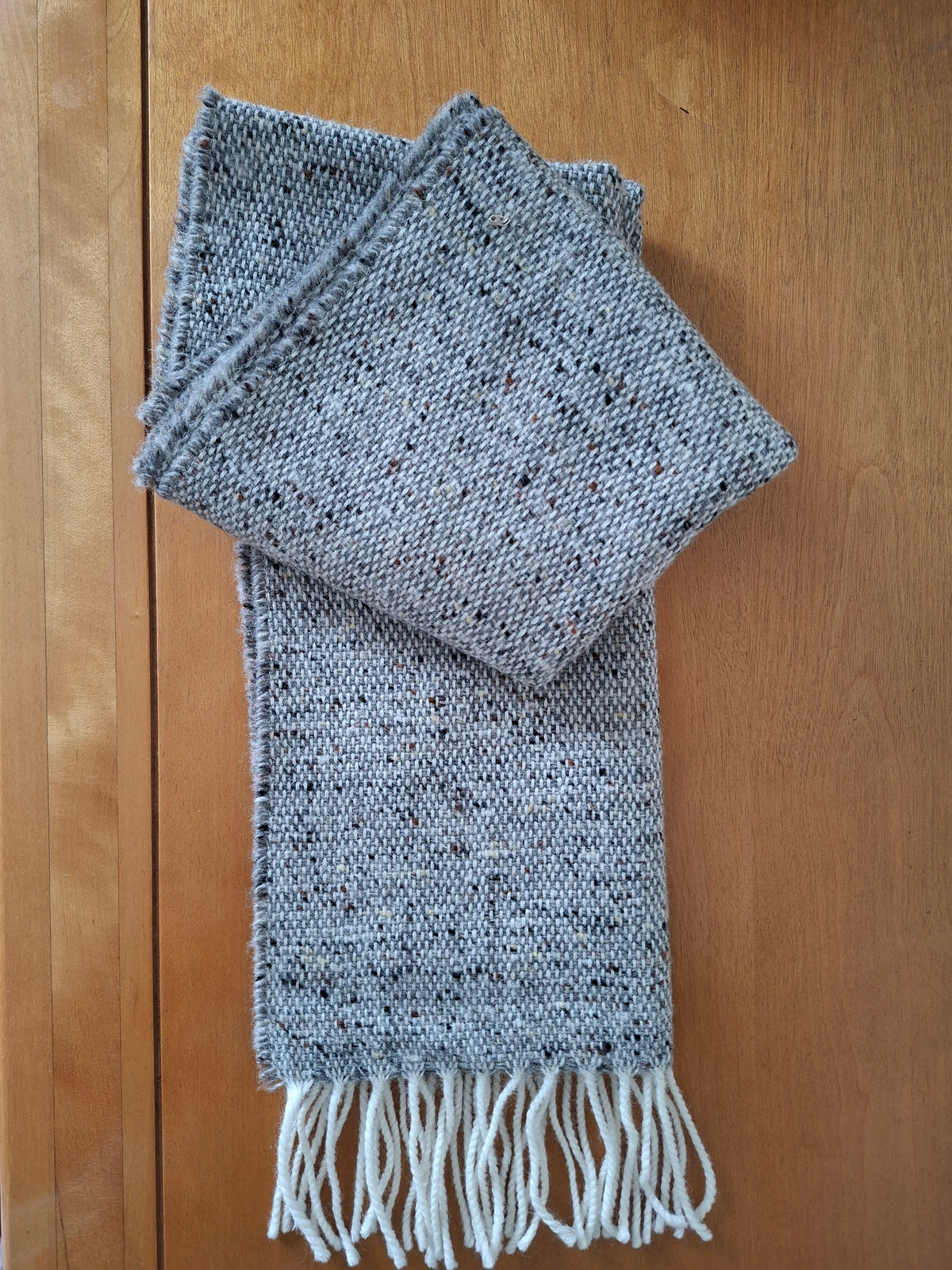 McNutt Donegal lambswool tweed scarf in donkey grey with off white fringe, folded on wooden background.