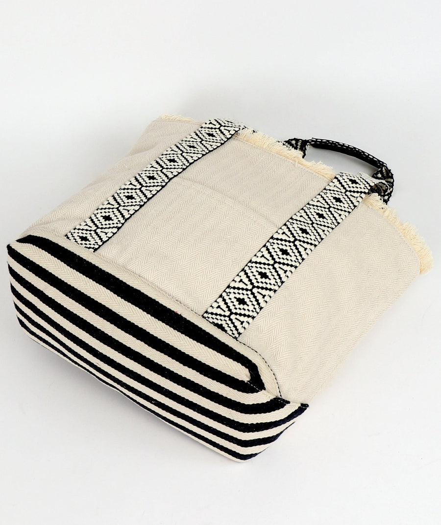 Side on view of off-white and black striped beach bag with geometric patterns by Pia Rossini on a white background