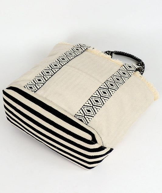 Side on view of off-white and black striped beach bag with geometric patterns by Pia Rossini on a white background
