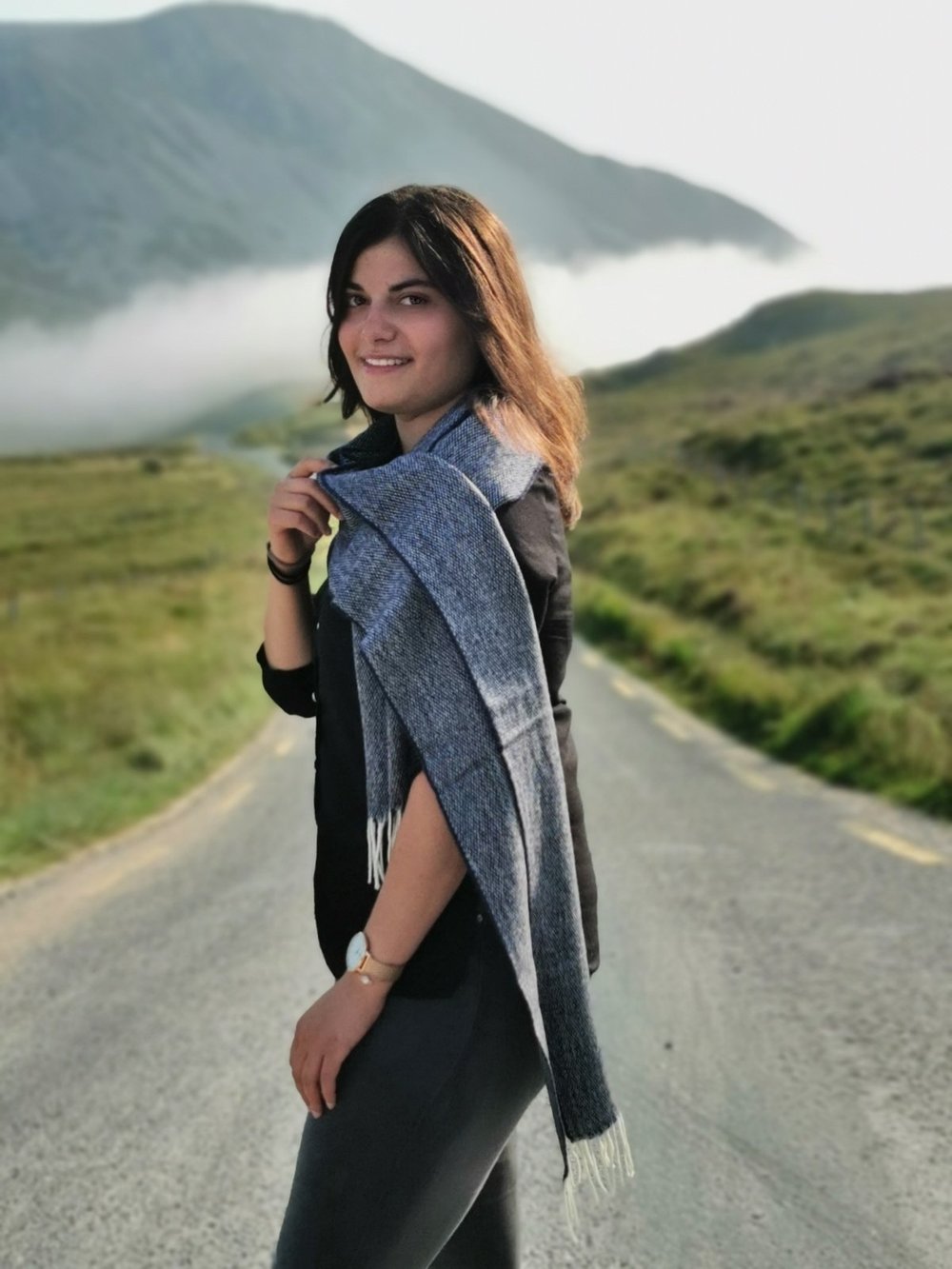 Lady wearing McNutt Donegal lambswool tweed scarf in navy standing on country road, natural Donegal landscape background 
