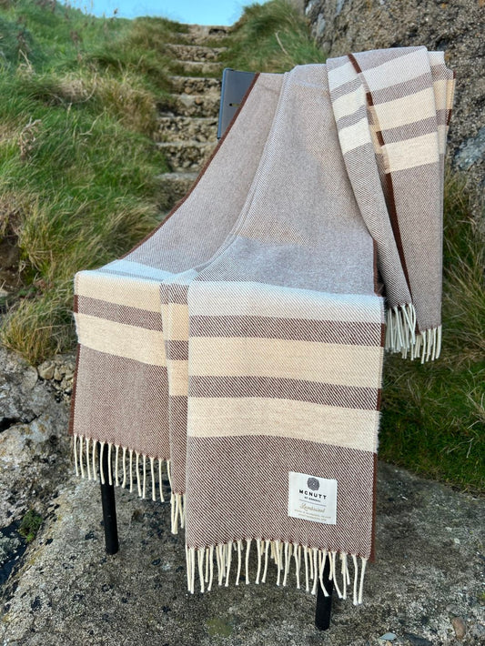 McNutt of Donegal Coffee Brew Merino lambswool throw displayed outdoors, showing brown and cream bands and fringed edges