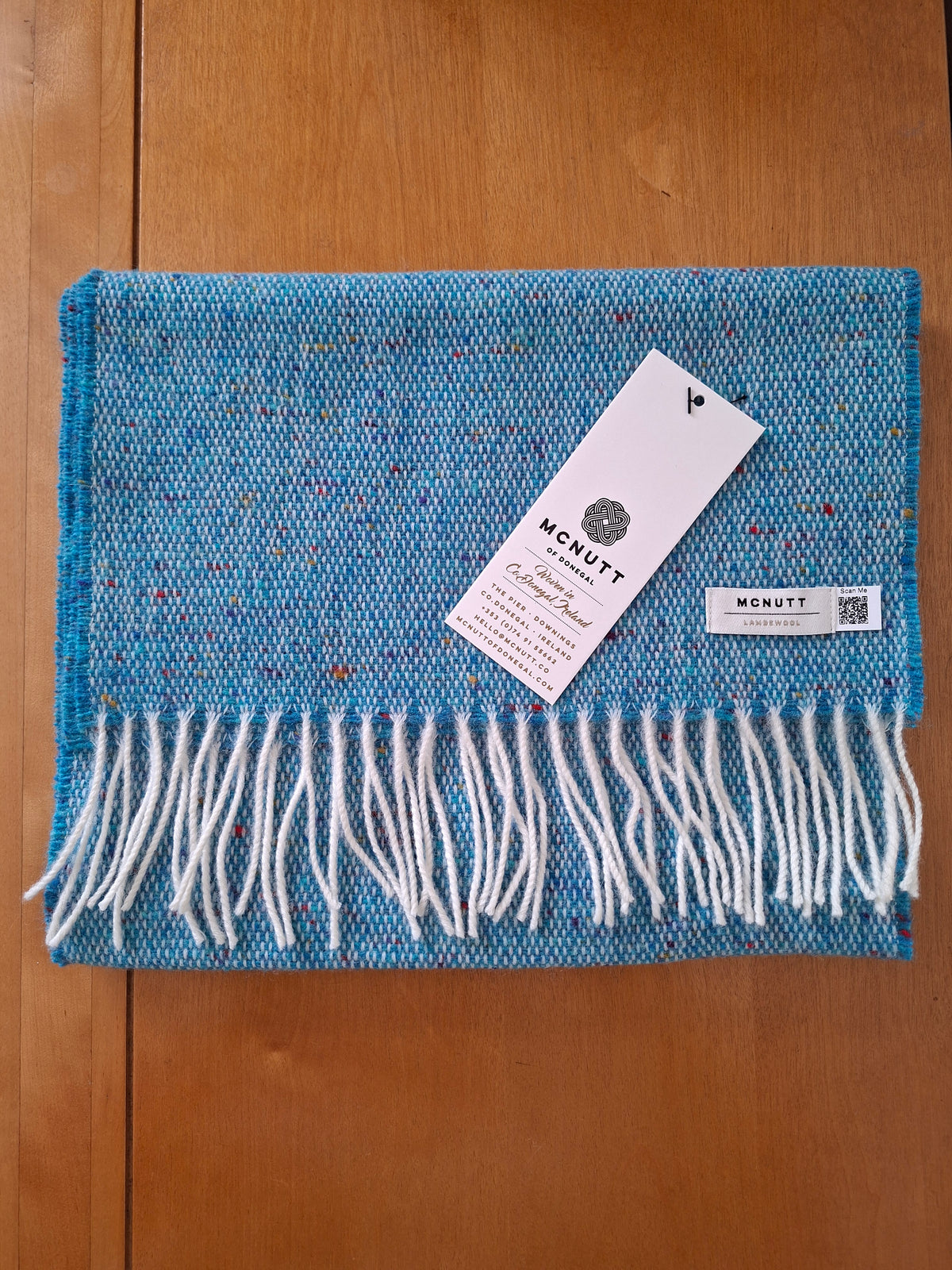 McNutt Donegal lambswool tweed scarf in Peacock with off white fringe, folded on wooden background.