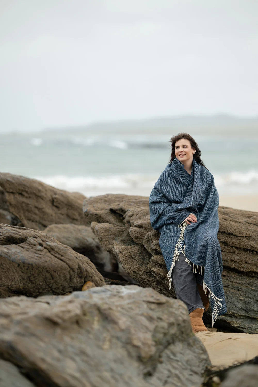 Woman wrapped in the McNutt Arranmore lambswool tweed throw on the rocky Donegal coast