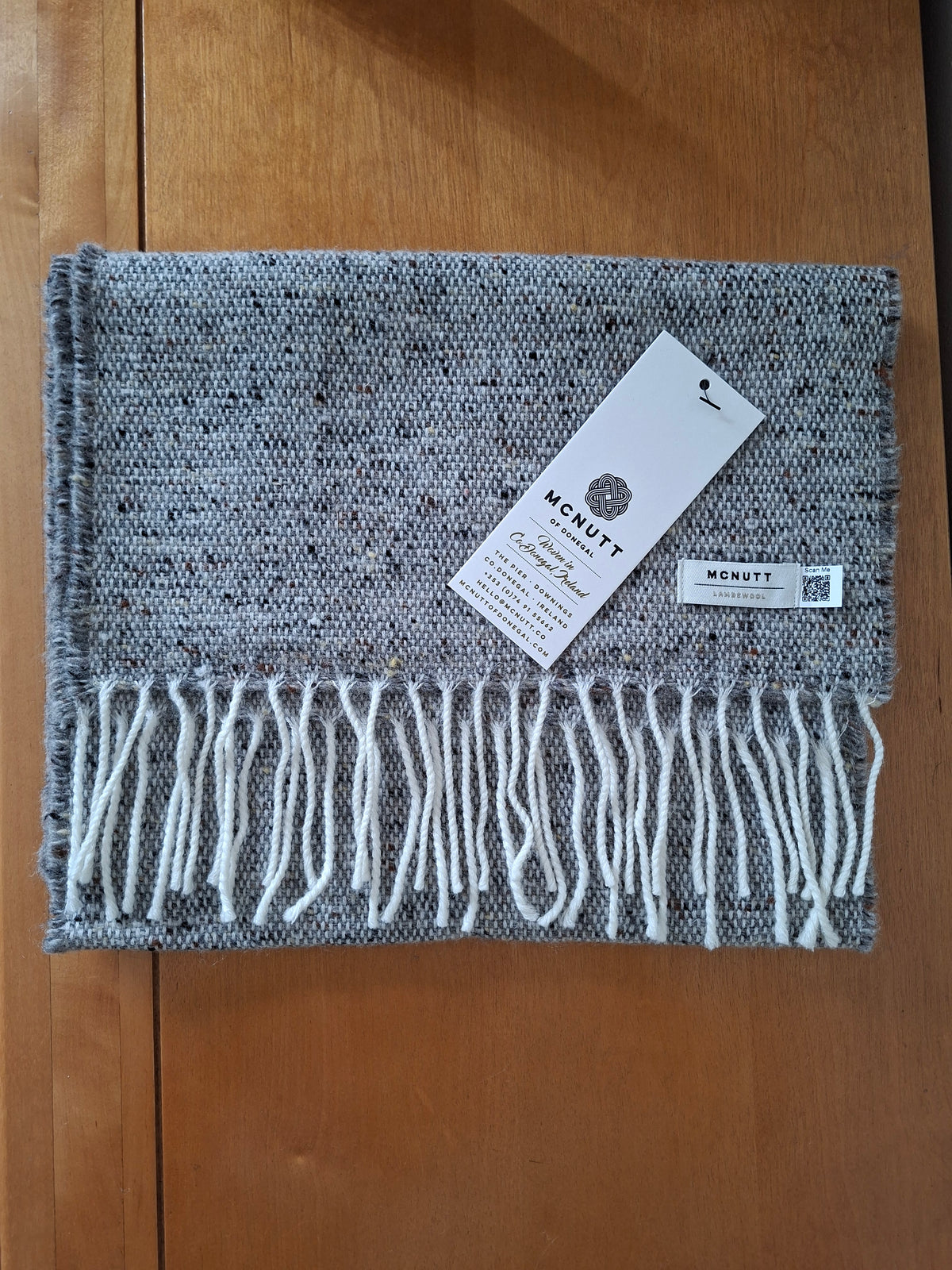McNutt Donegal lambswool tweed scarf in donkey grey with off white fringe, folded on wooden background.